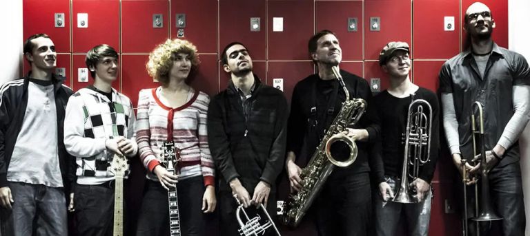 Gruppenfoto der Musiker*innen vor einer Wand mit roten Schließfächern