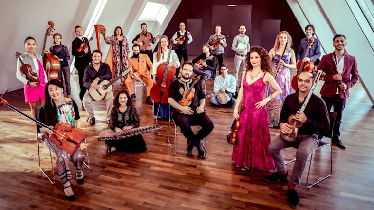 Gruppenfoto des locker gruppierten Ensembles in einem Raum mit schrägen Wänden