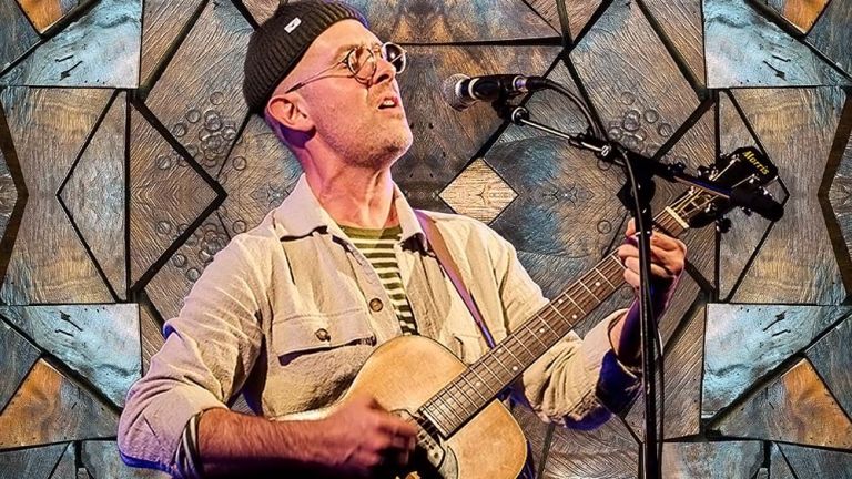 Der Musiker bei einem Soloauftritt vor einer künstlerisch mit Holz vertäfelten Wand