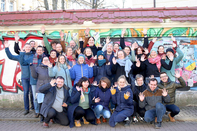 Fröhliches Gruppenfoto der Sängerinnen und Sänger vor einer Mauer mit einem bunten Graffiti