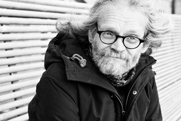 Der Autor sitzt mit Winterjacke und Schall mit nachdenklichem Blick im Freien auf einer Bank.