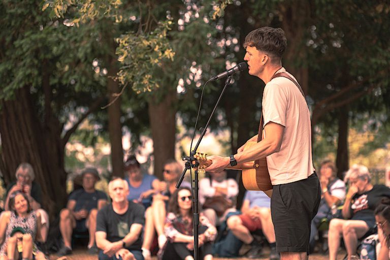 Der Sänger spielt ein Freiluftkonzert und sein Publikum sitzt eintspannt auf einer Wiese.