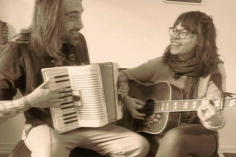 Die beiden Musiker mit Akkordeon und Gitarre lächeln sich bei einem Konzert an.