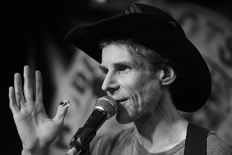 Foto des freundlich blickenden Sängers mit Drei-Tage-Bart und Cowboyhut bei einem Konzert