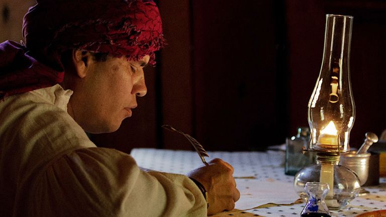 Filmszene, in der man Sequoyah an einem Tisch mit Petroleumlampe und mit einer Feder schreibend sitzen sieht