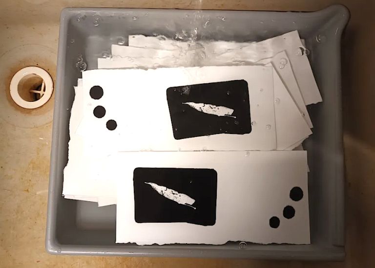 In einem Spülbecken steht eine Schale mit Photogrammen, in die Wasser läuft