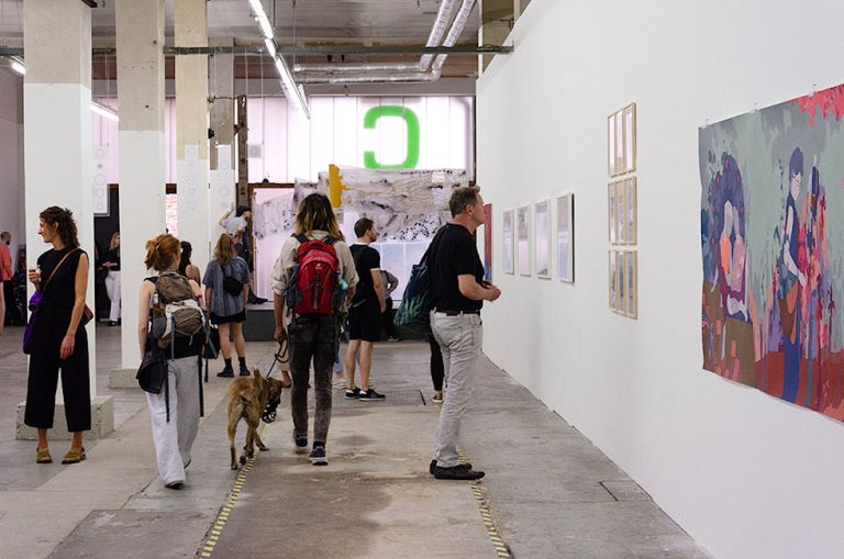 In einer ehemaligen Fabrikhalle schauen sich Besucherinnen und Besucher eine Ausstellung an.