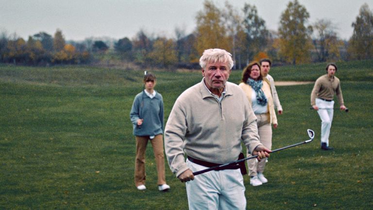 Eine Gruppe von Golfspieler*innen läuft mit ernstem Gesicht und den Golfschlägern in der Hand auf den Betrachter zu.