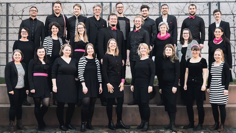 Gruppenfoto des Chors in schwarzer, teils schwarz-weiß gestreifter, Auftrittskleidung