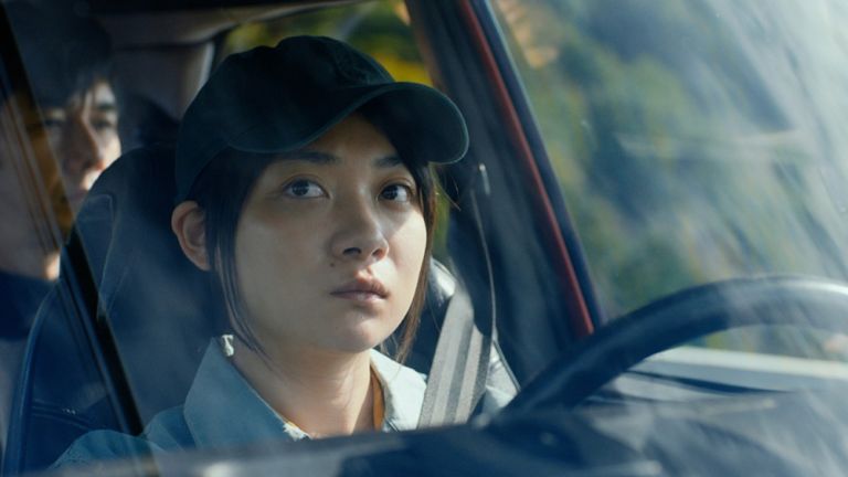 Eine junge Frau fährt Auto und sieht ihren Fahrgast durch den Rückspiegel an.