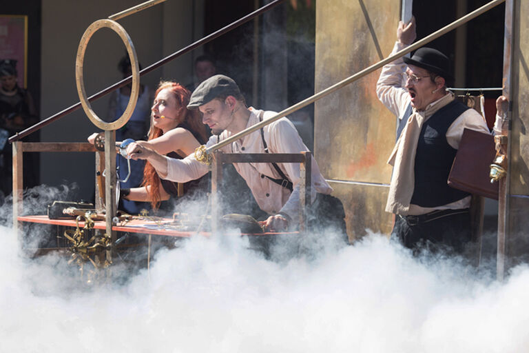 Zwei Schauspieler und eine Schauspielerin stehen in viel Nebel vor etwas, das die Komandobrücke eines Raumschiffes sein könnte.