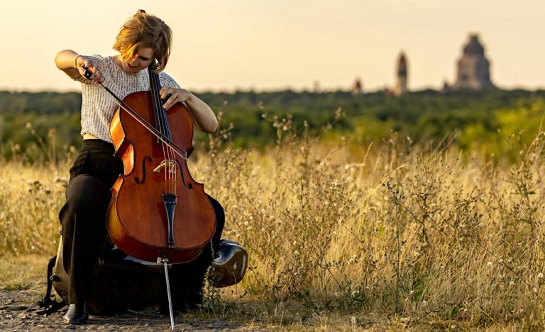 Foto der Musikerin, die auf einer Wiese Cello spielt
