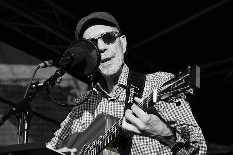 Schwarz-Weiß-Foto des Musikers, der bei einem Auftritt singt und Gitarre spielt.