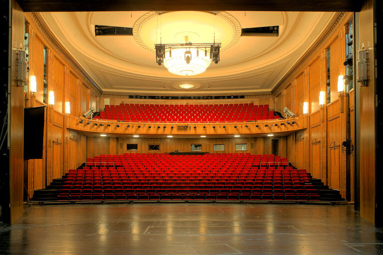 Blick in den leeren holvertäfelten Saal mit seinen roten Sesseln von der Bühne aus