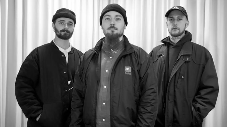 Schwarz-Weiß-Foto der Band in Straßenkleidung vor einem hellen Vorhang