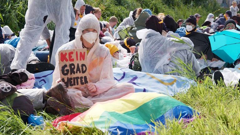 Klimaaktivist*innen haben sich in Schutzanzügen auf einer wiese niedergelassen.