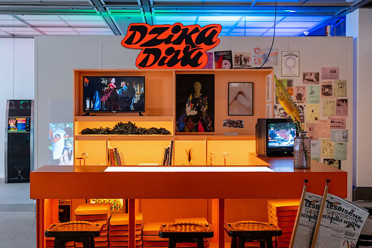 Foto eines Bartresens mit zwei Bildschirmen und Fotos sowie Zeitungsartikeln an den Wänden