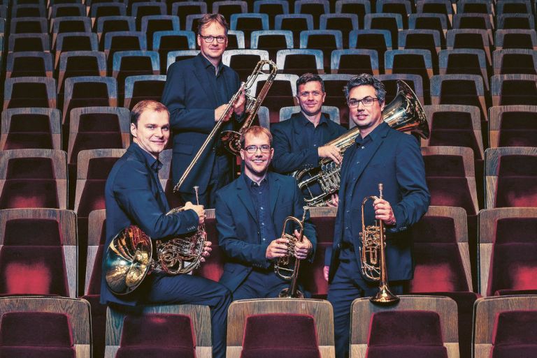 Gruppenfoto der fünf Musiker mit ihren Instrumenten zwischen den Stuhlreihen im Gewandhaus