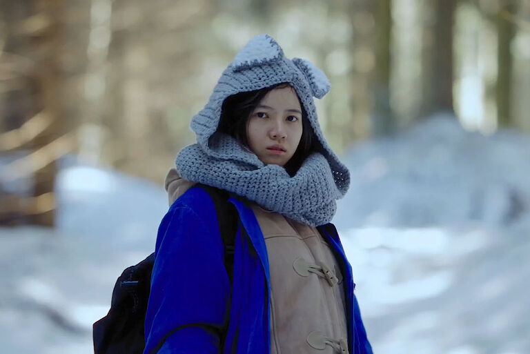 Eine junge Frau in warmer Kleidung läuft durch einen verschneiten Wald.