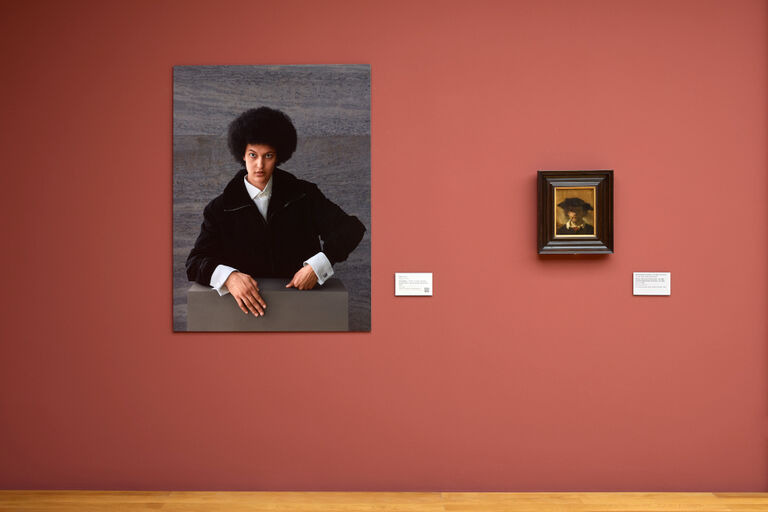 Das großformatige Porträtfoto einer Frau hängt neben dem kleinen Gemälde eines Mannes.