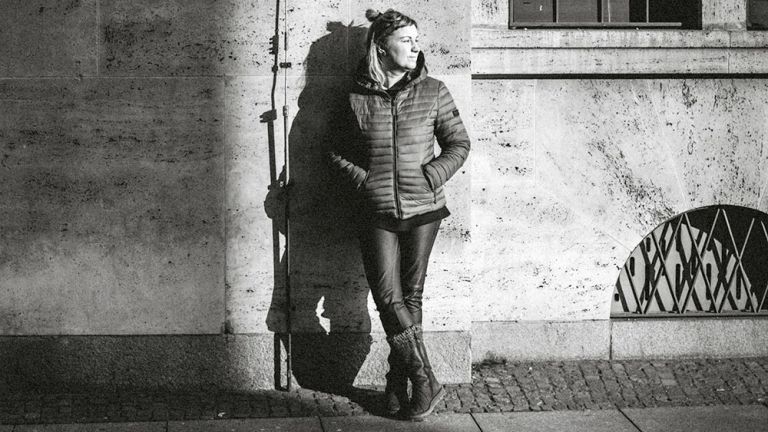 Schwarz-Weiß-Foto der Künstlerin, die nachts allein auf der Straße an einer Hauswand lehnt