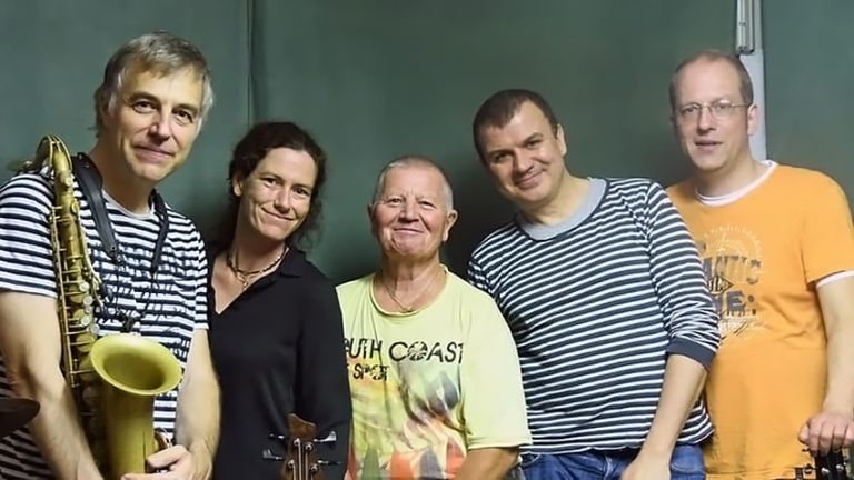 Gruppenfoto des freundlich lächelnden Quintetts vor einer grünen Wand