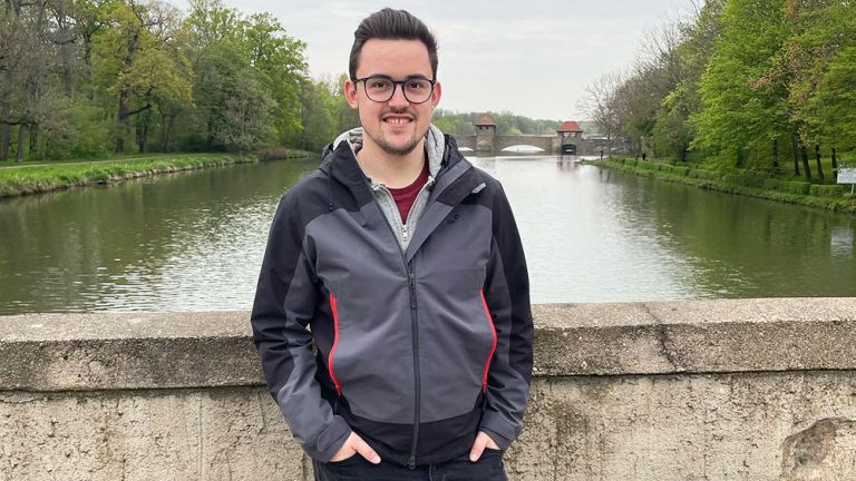 Der junge Musiker steht entspannt lächelnd an ein Brückengeländer gelehnt.