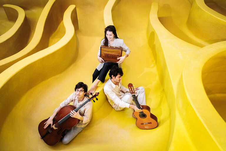 Gruppenfoto des Trios mit seinen Instrumenten in einem zitronengelben Labyrinth