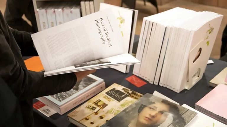 Eine Person blättert vor einem großen Bücherstand in einem Fotobuch.