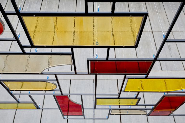 In einem hohen Lichthof des Museums hängt parallel zur Decke eine Stahlgitter mit gelben und roten Glasscheiben