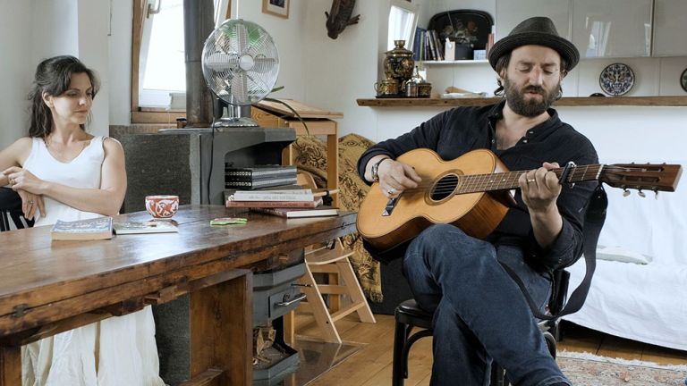 Susan Sideropoulos und ein Mann mit Hut der Gitarre spielt sitzen an einem alten Holztisch.