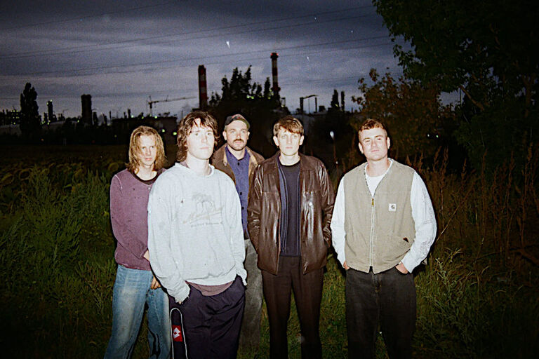 Ein Gruppenfoto der Band, aufgenommen nachts mit der Silhouette einer Stadt im Hintergrund