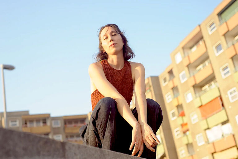 Foto der Sängerin, in einem Plattenbauviertel und schräg von unten aufgenommen