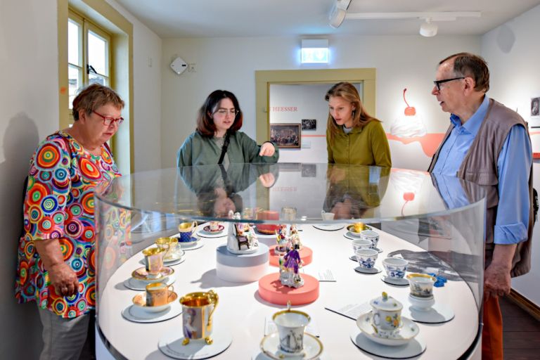 Besucher und Besucherinnen stehen um eine große Glasvitrine mit historischen Kaffeetassen und Porzellanfiguren