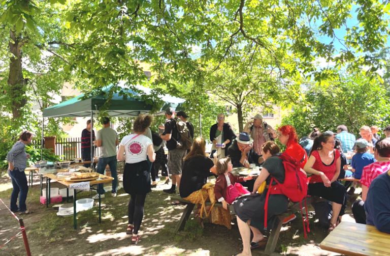 Viele Menschen in einem grünen Hof mit Ständen und Tischen und Bänken