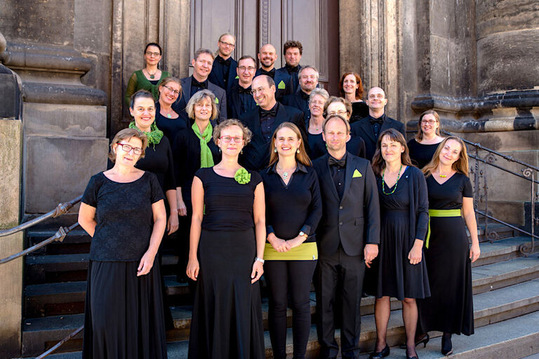 Gruppenfoto des Chores auf einer Kirchentreppe in schwarzer Auftrittskleidung mit limetten-grünen Akzenten wie Schals, Anstecker oder Einstecktücher