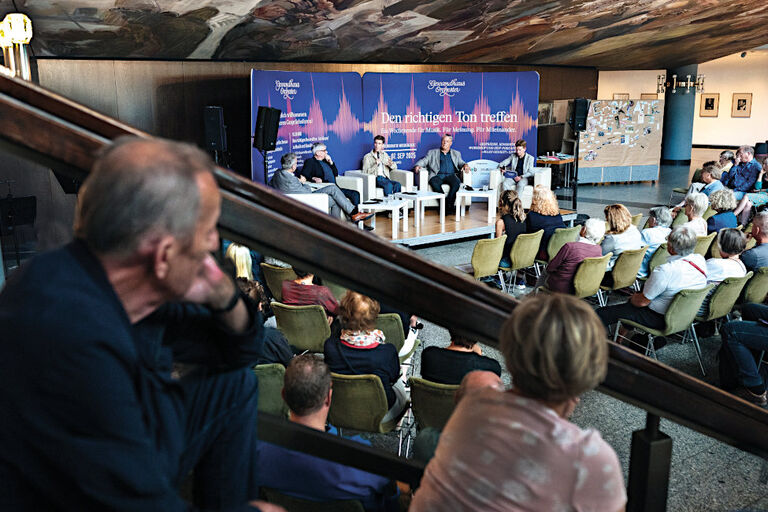 Im Foyer des Gewandhauses verfolgen viele Menschen auf Stühlen und Treppen sitzend eine Podiumsdiskussion