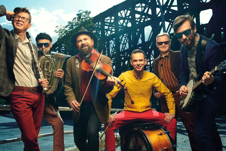Gruppenfoto der Musiker mit ihren Instrumenten vor einer Brücke