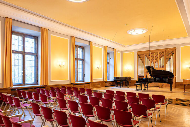 Blick in den historischen Kammermusiksaal mit Konzertflgel und Orgel sowie Reihen mit riten Stühlen