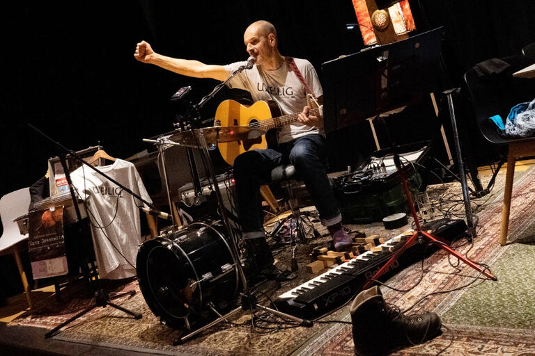 Der Multiinstrumentalist sitzt bei einem Konzert zwischen seinen vielen Instrumenten auf der Bühne.