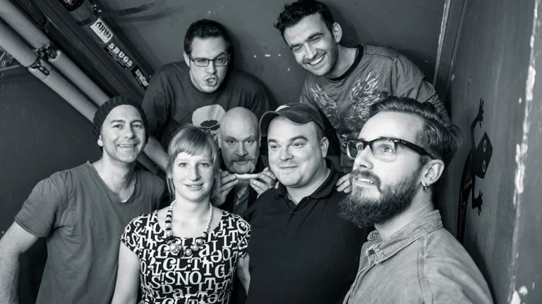 Schwarz-Weuß-Gruppenfoto der siebenköpfigen Band in einem engen Kellergang