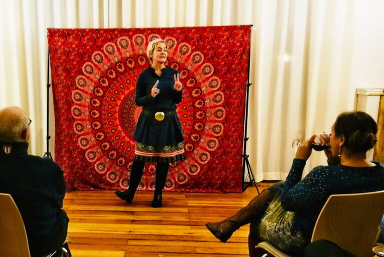 Die Erzählerin führt ein Programm vor einem roten Wandteppich vor.