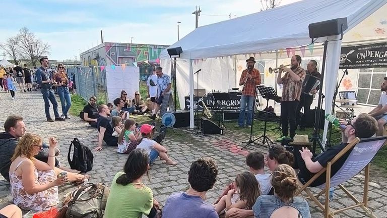 Kleine und große Zuschauer sitzen in Liegestühlen oder auf dem boden und lauschen einem Konzert beim Stadtteilfest.
