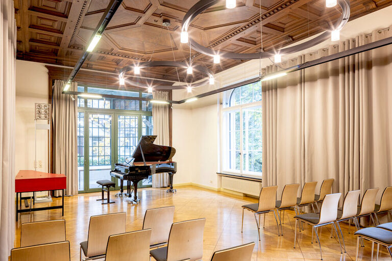 Blick in einern hellen Musiksalon mit Konzertflügel und großen Fenstern.