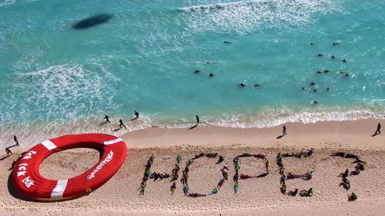 Luftaufnahme eines Strandes, auf dem viele Menschen den Schriftzug "Hope?" formen