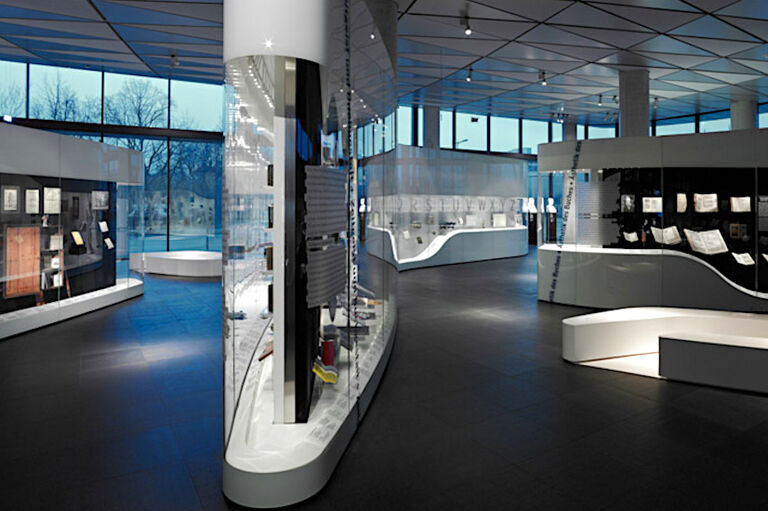 Ein Ausstellungsraum mit einer breiten Glasfront nach außen, vielen Glasvitrinen und Sitzgelegenheiten