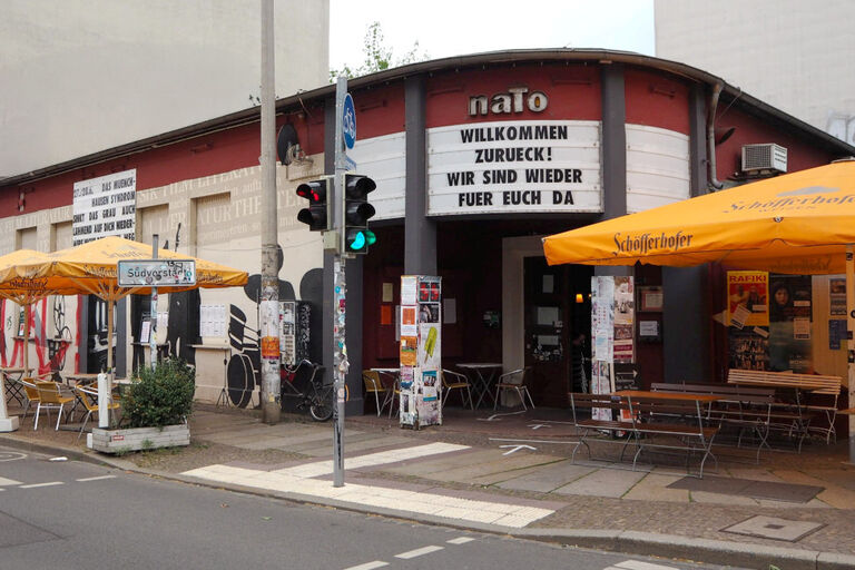 Das Gebäude der naTo mit Freisitz und Sonnenschirmen davor und mit dem Spruch "Willkommen zurück! Wir sind wieder für euch da" über dem Eingang
