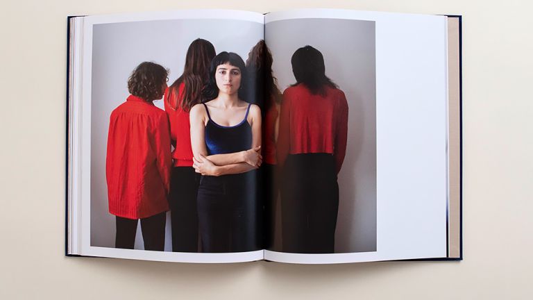 Auf der Doppelseite eines Buches ist eine Foto mit fünf Frauen zu sehen. Vier von ihnen, in roter Kleidung, stehen mit dem Rücken zum Betrachter, während eine direkt in die Kamera schaut.