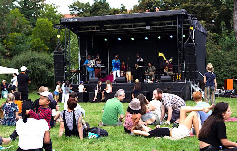 Viele Menschen sitzen auf einer Wiese vor einer Bühne und verfolgen ein Konzert.