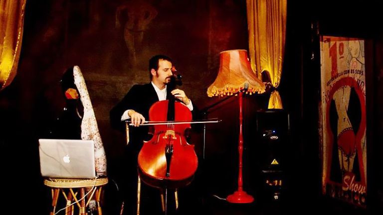 Der Musiker sitzt bei einem Konzert mit seinem Cello und einem Laptop auf der Bühne.